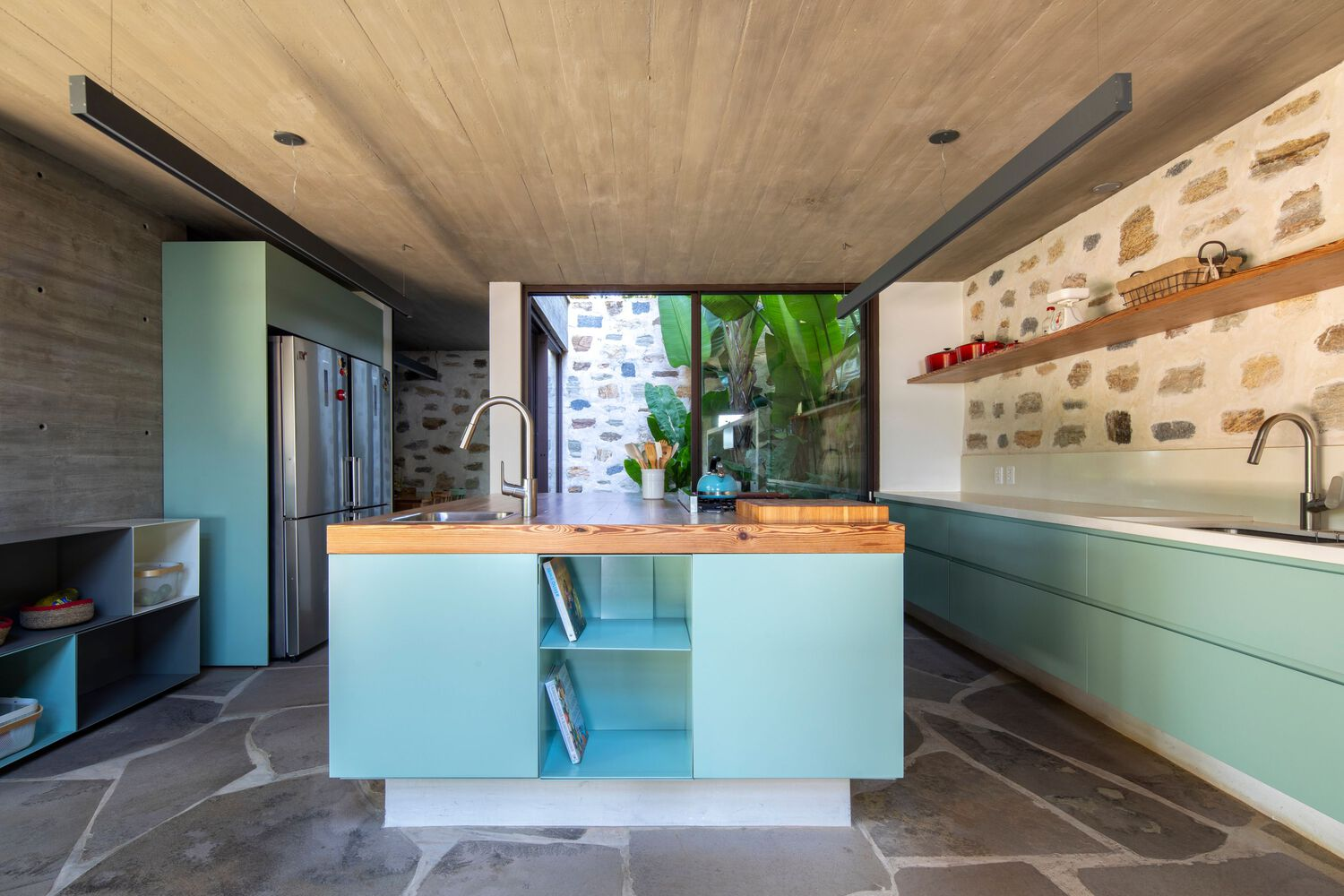 Kitchen with pale blue cabinetry, timber countertop island, and rubble stone wall beneath concrete ceiling