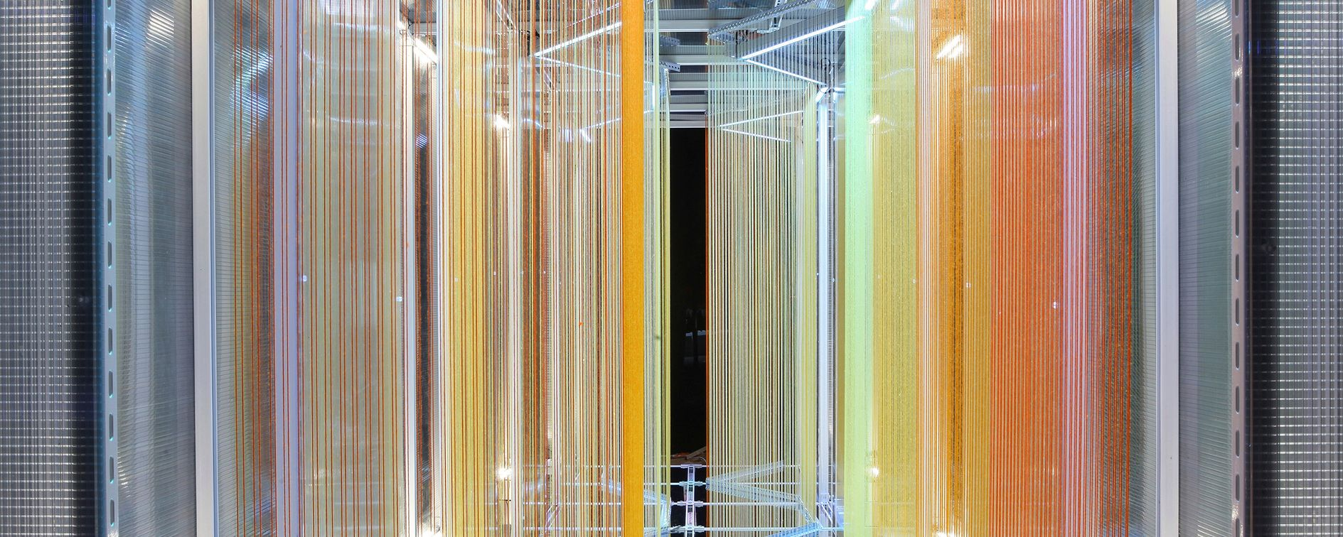 A colorful array of vertical threads creating a vibrant, immersive passage where light, color, and structure merge into an architectural art form.