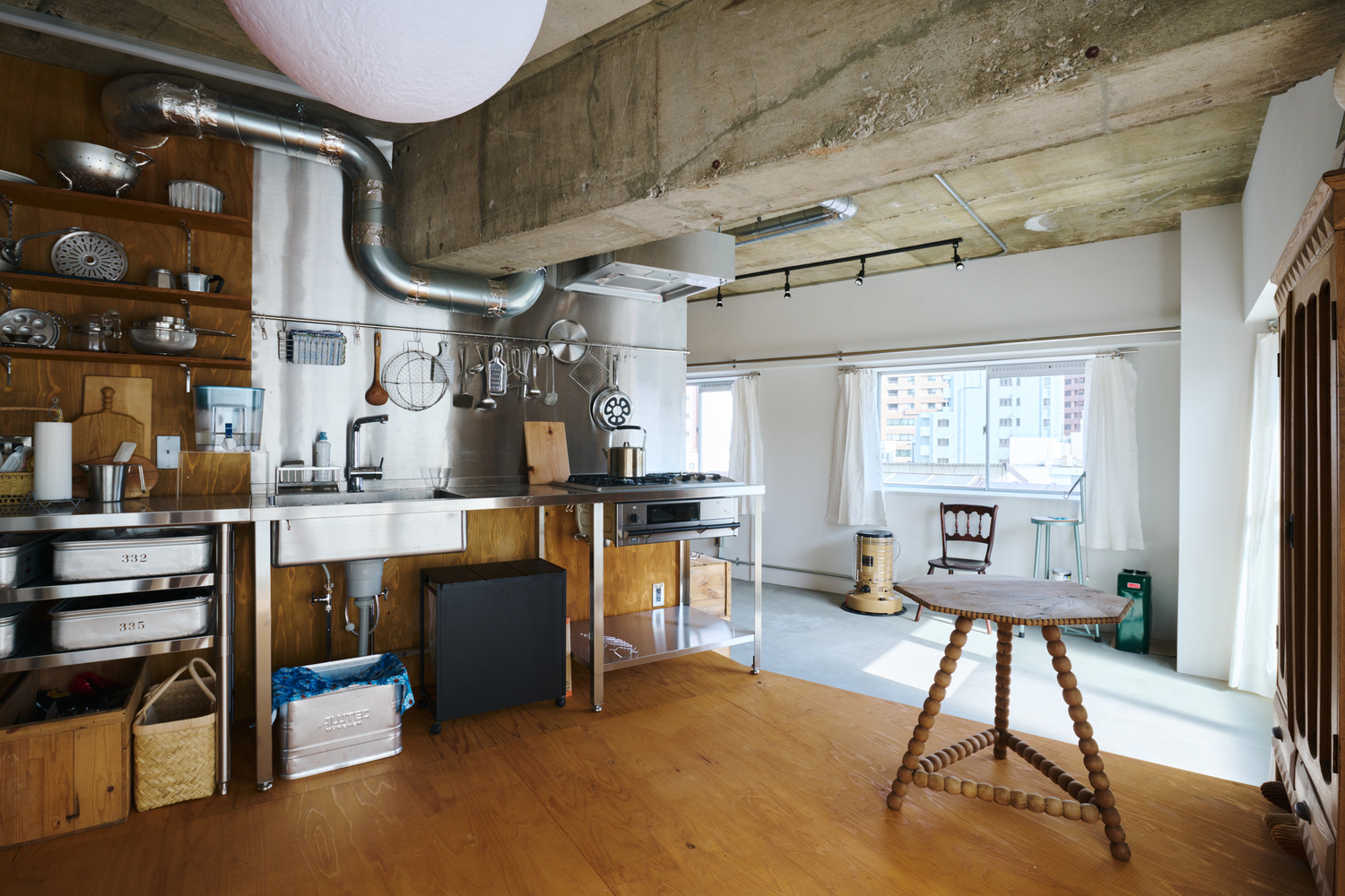 Open plan living space with exposed concrete ceiling, industrial ducting, and timber kitchen in afternoon light