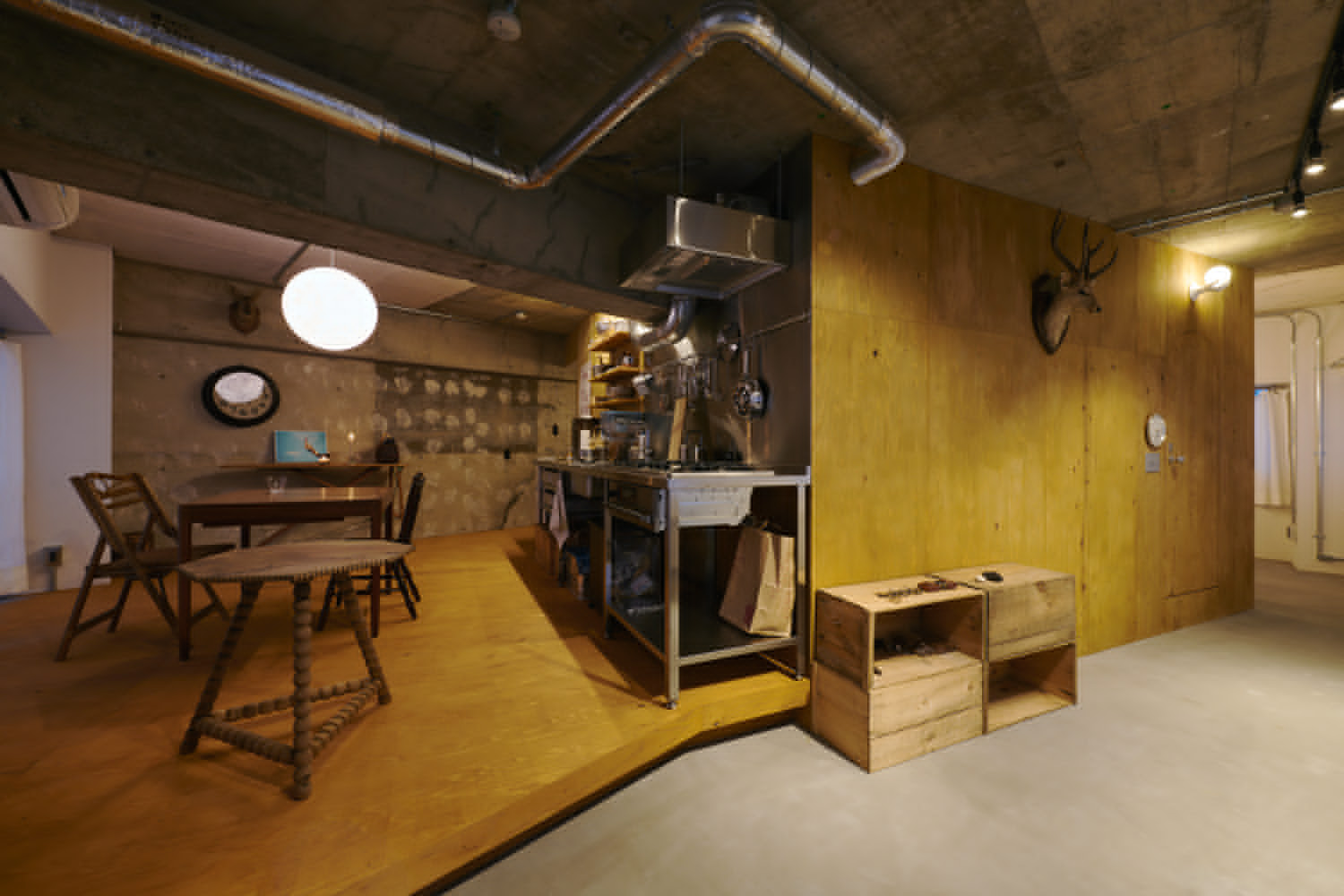 Dining area with concrete ceiling, plywood storage boxes, and exposed ductwork under warm artificial lighting