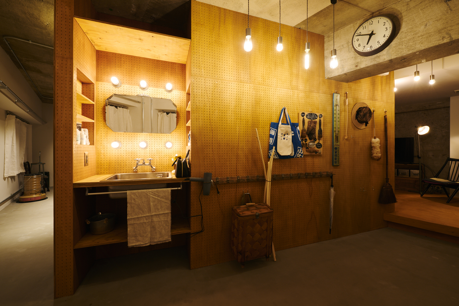 Bathroom vanity with perforated plywood panels, pendant bulbs, and wall clock at evening