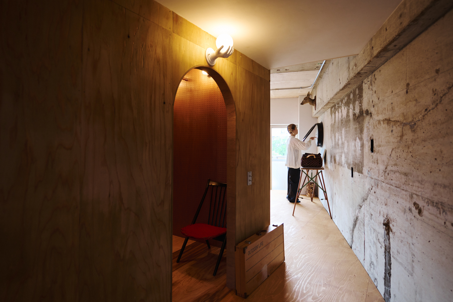 Narrow hallway with person on ladder beside board-formed concrete wall and plywood storage volume
