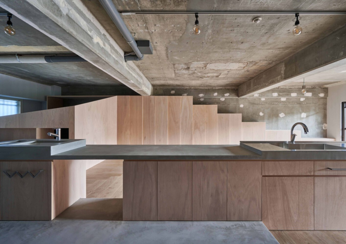 Kitchen island with timber cabinetry and dark countertop beneath exposed concrete ceiling with track lighting