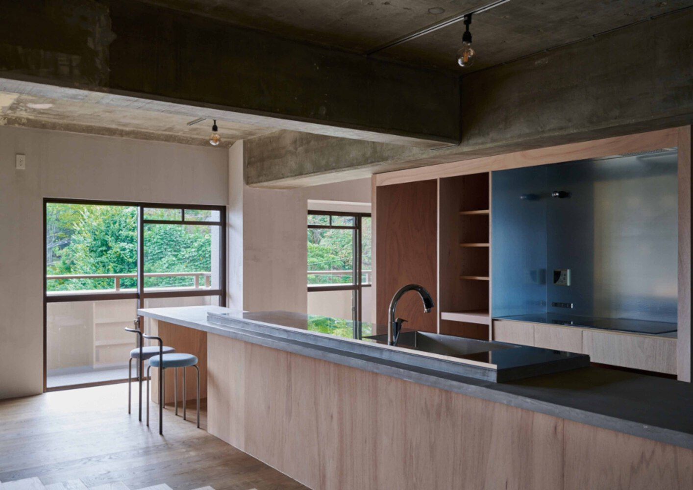 Open kitchen with light wood cabinetry and exposed concrete ceiling beams overlooking a green balcony