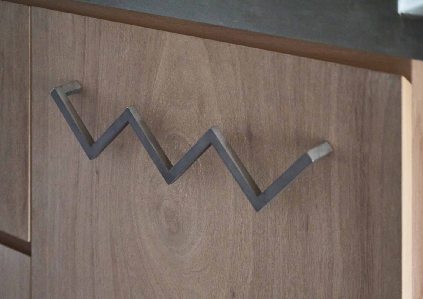 Close-up of a zigzag steel coat hook mounted on a light wood cabinet door