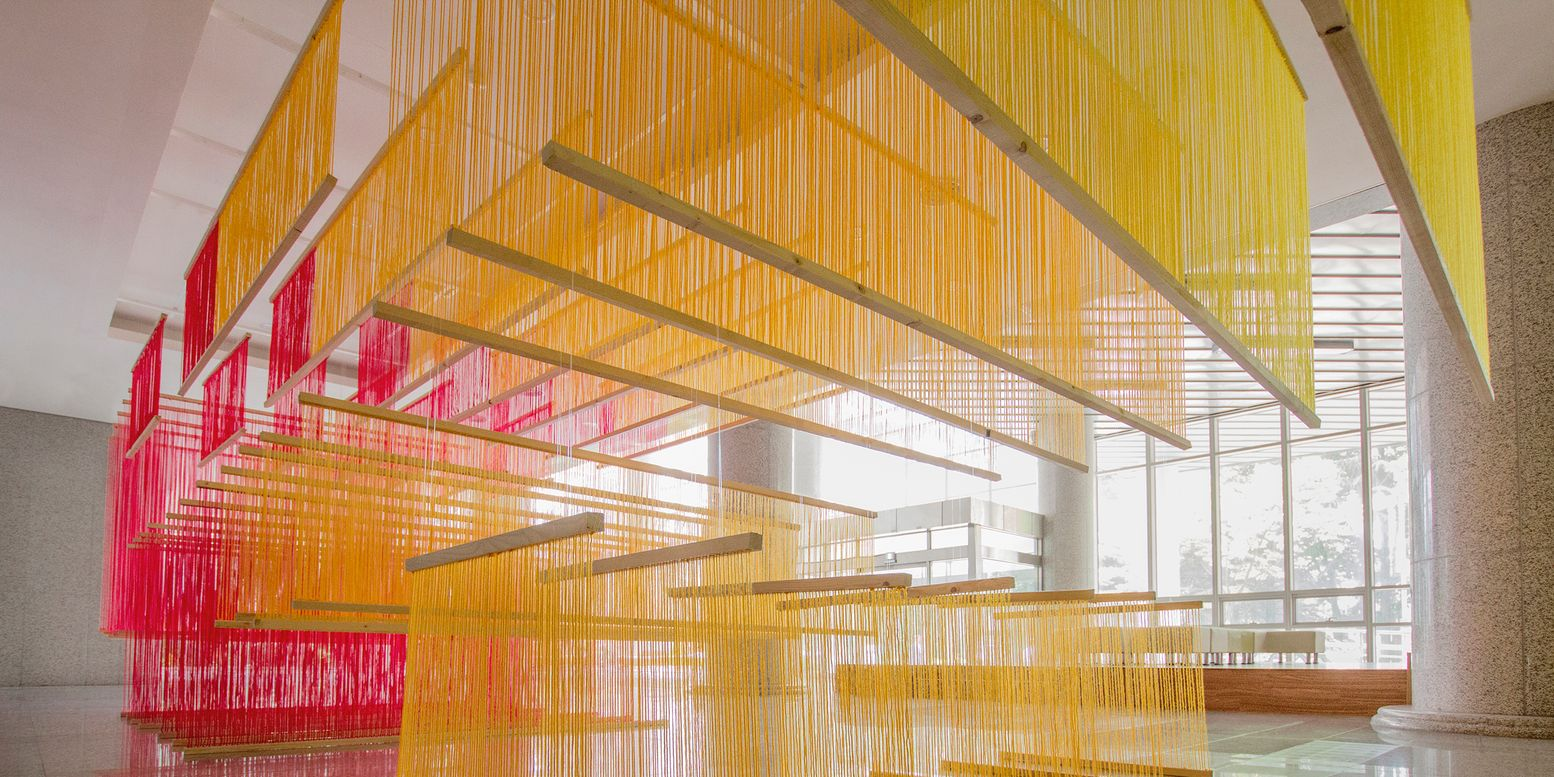 Suspended thread installations forming geometric volumes beneath a white coffered ceiling near glazed walls