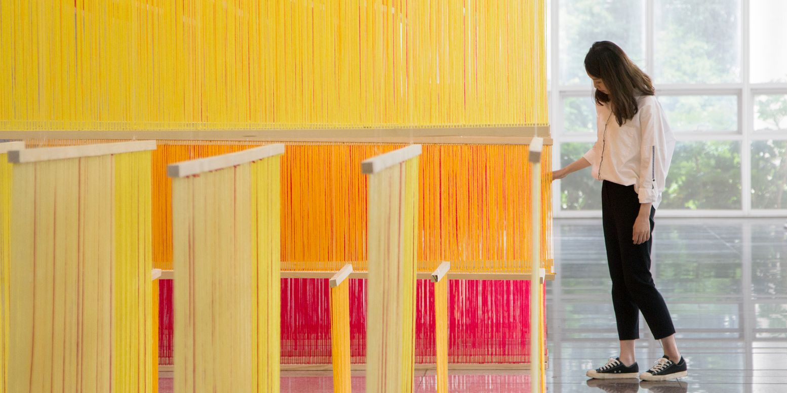 Yellow and orange layered string installation with a visitor approaching the glazed wall