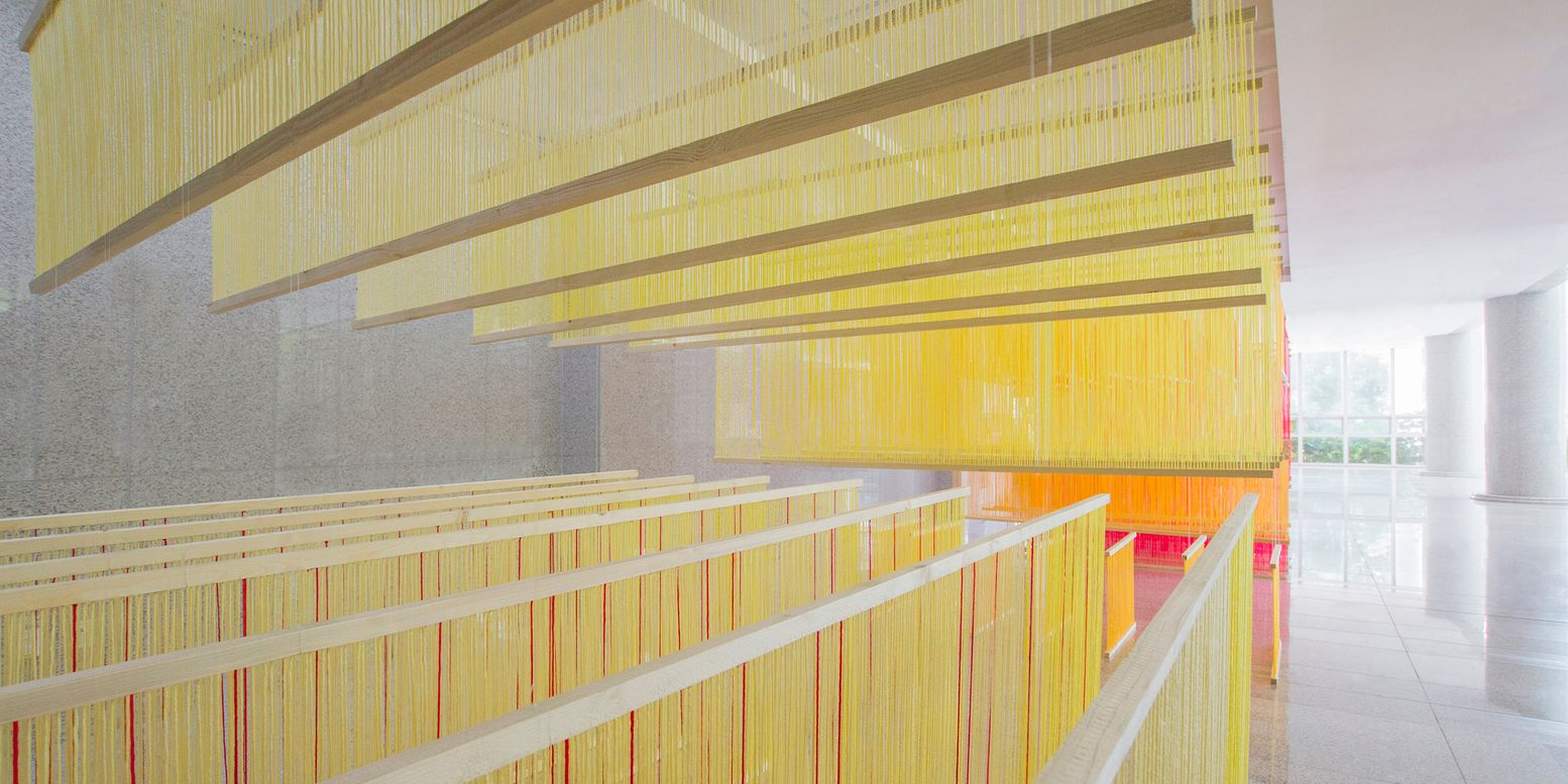 Angled view of the tiered yellow string installation reflecting on the polished floor