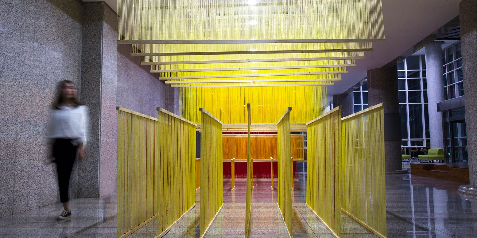 Entry passage through the yellow string installation with a blurred figure walking in the lobby at dusk