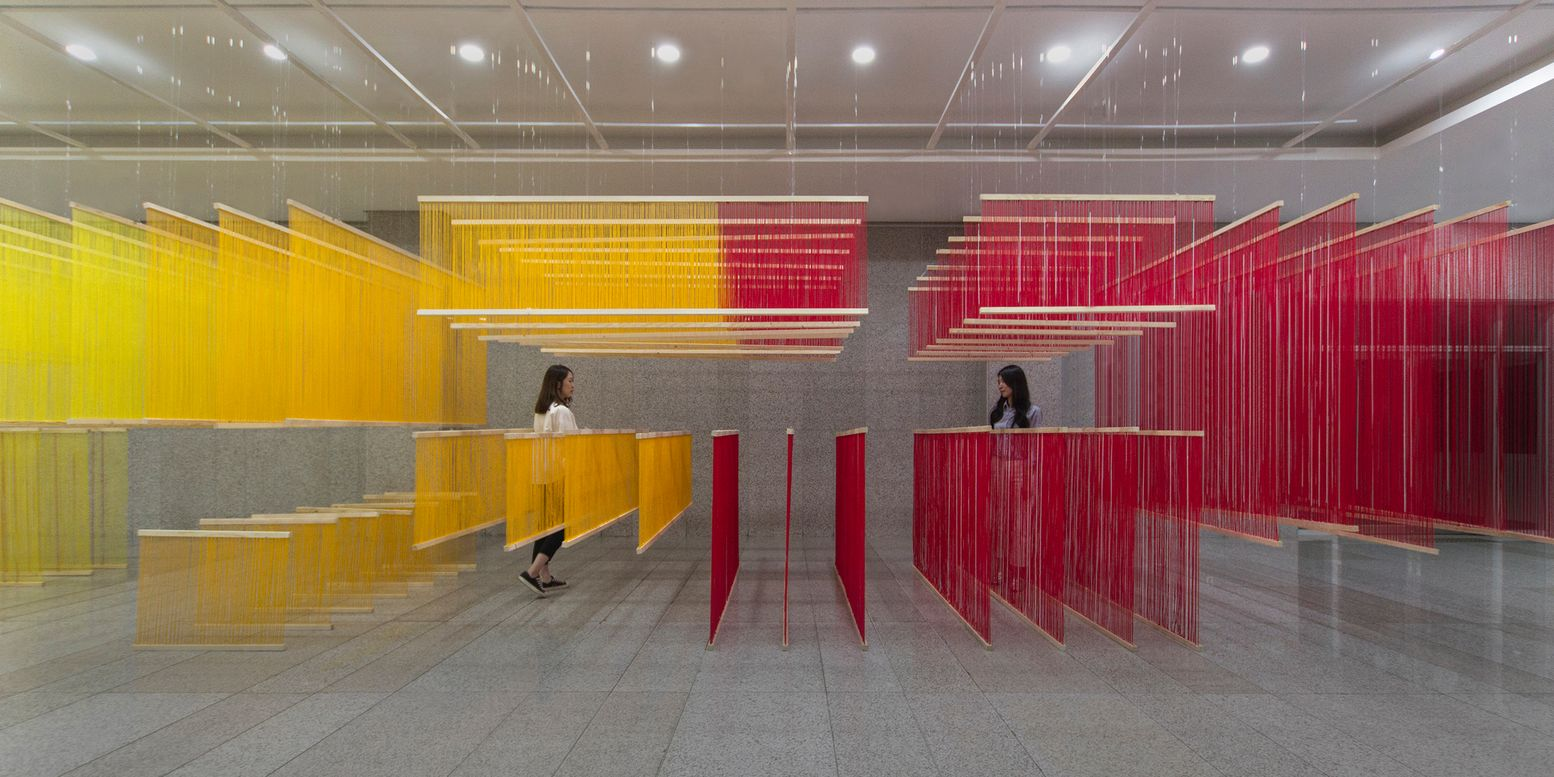Wide view of the thread panel installation with two visitors moving through the layered spatial dividers