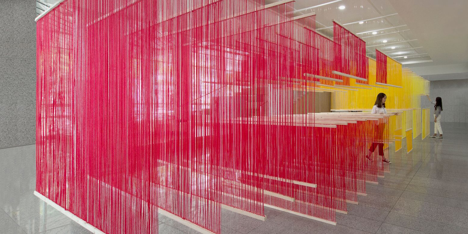 Layered suspended panels of pink and yellow thread creating translucent partitions in a lobby