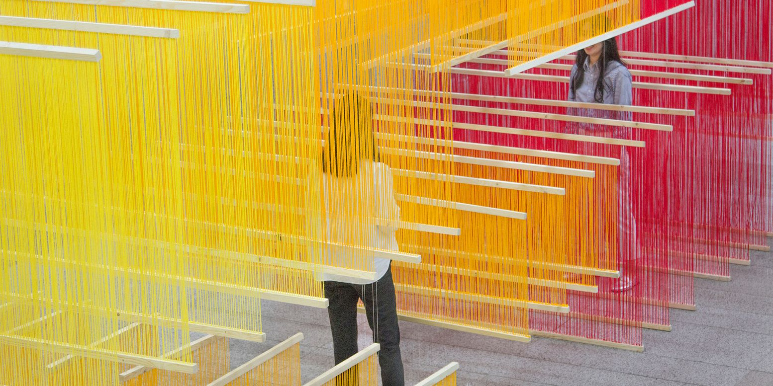 Close view through overlapping colored thread panels with a visitor visible between the layers