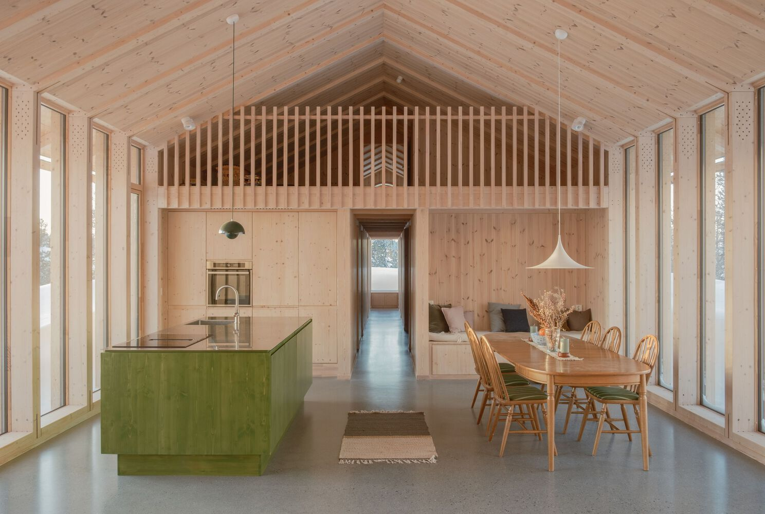 Open-plan interior with green kitchen island, exposed timber rafters and vertical slat partition at the gable end