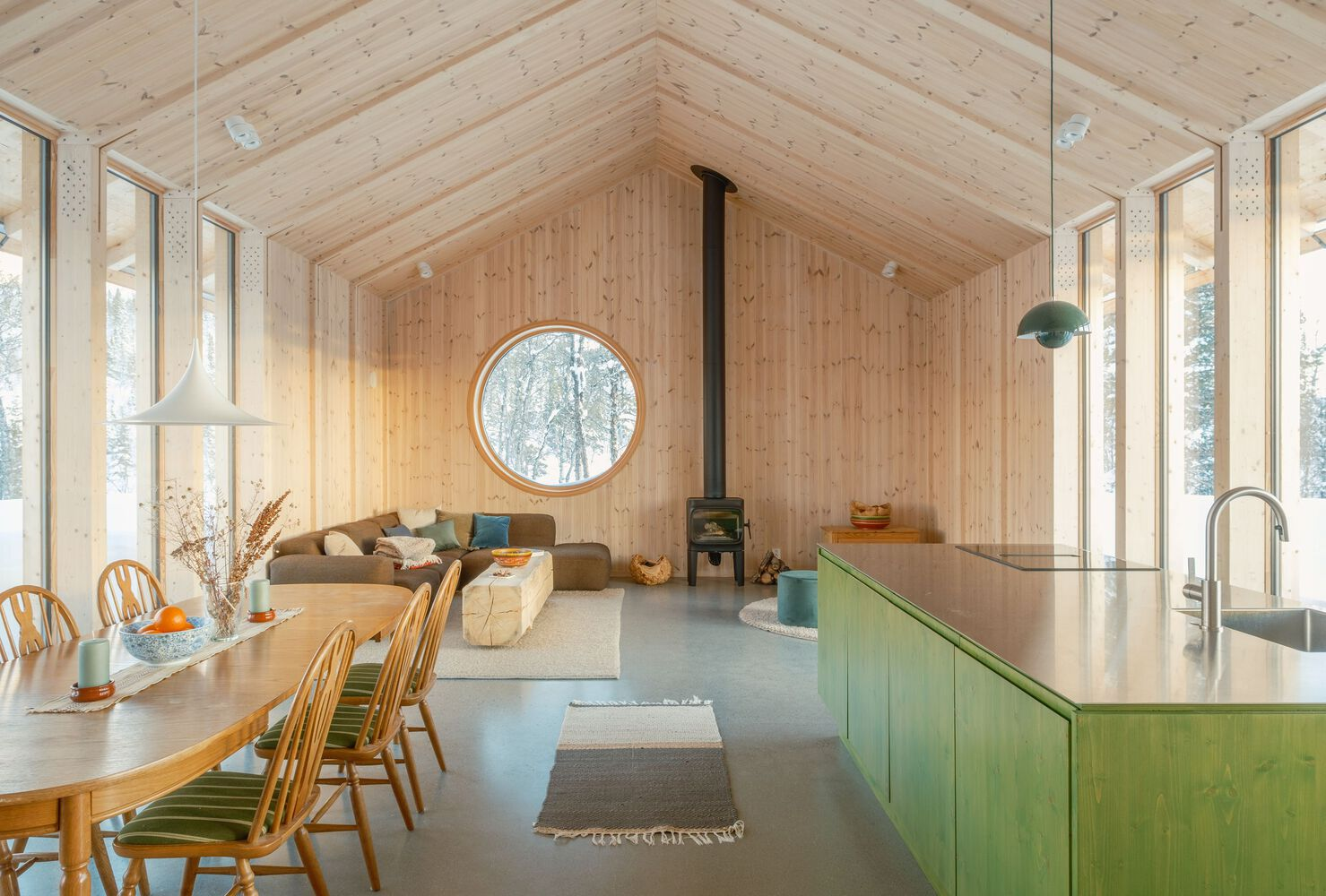 Interior view across green kitchen island toward living area with circular window and tall glazed walls on both sides