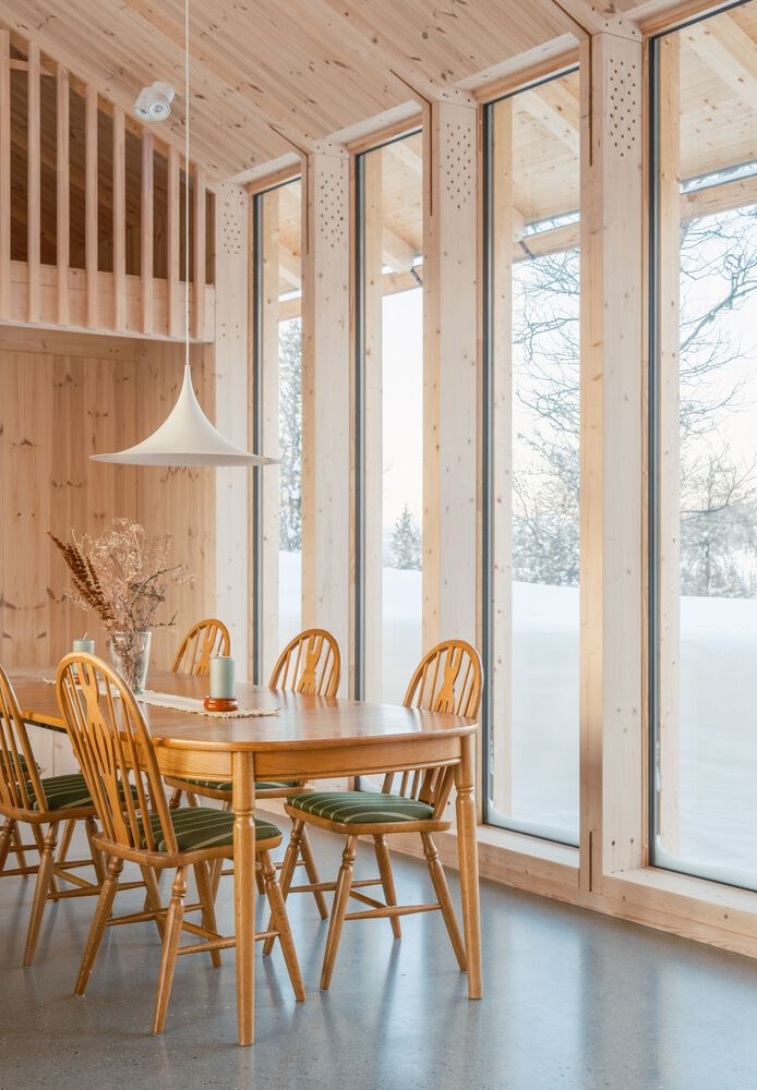 Dining area with tall timber-framed windows overlooking a snowy landscape with bare trees