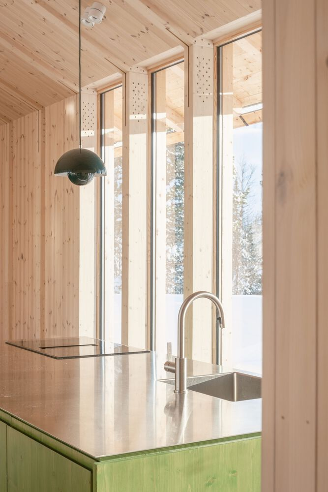 Kitchen counter with green cabinetry and polished metal sink facing a snowy winter scene