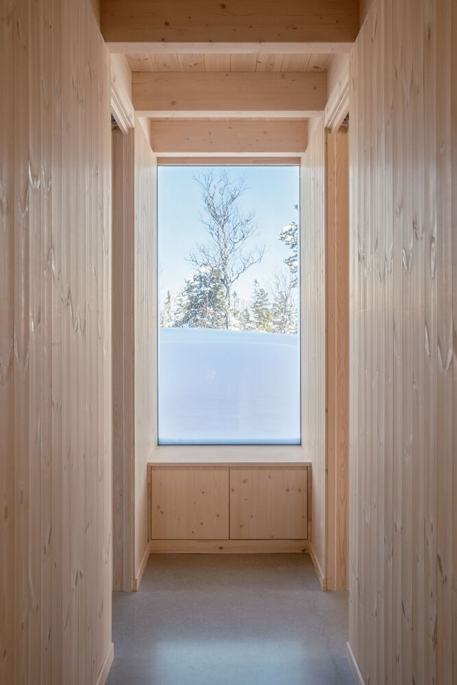 Narrow timber-lined corridor with built-in storage cabinet beneath a window framing snow and trees