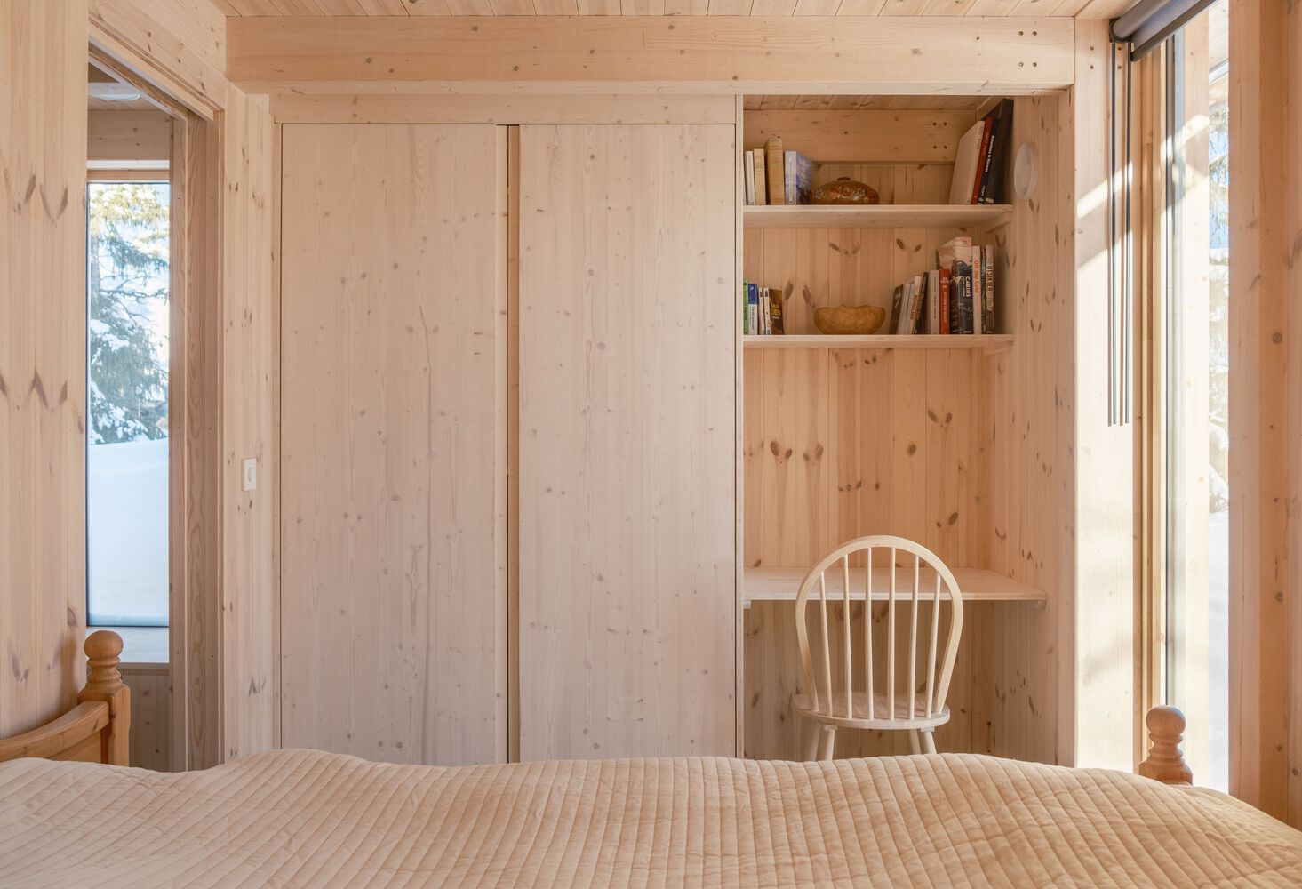 Bedroom with pale timber walls, flush cabinetry and built-in desk nook beside the bed