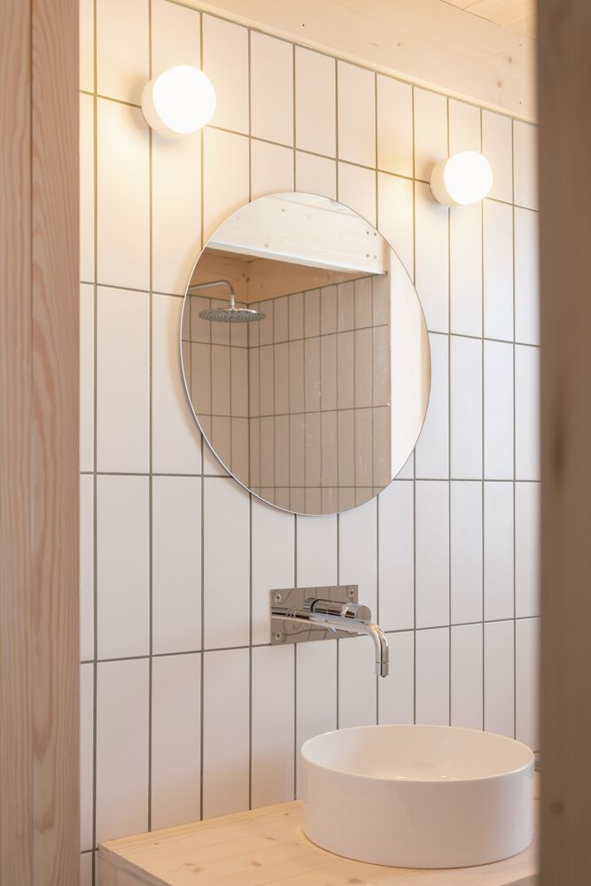 Bathroom vanity with round mirror against white vertical tile and globe sconces flanking the sink