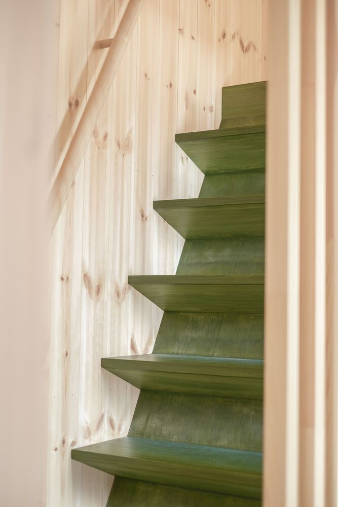 Green-stained timber staircase with cantilevered treads against pale wood paneling