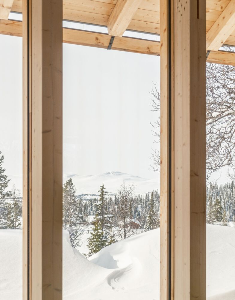 Floor-to-ceiling window framed by timber columns and rafters overlooking snow-covered forest and distant mountains