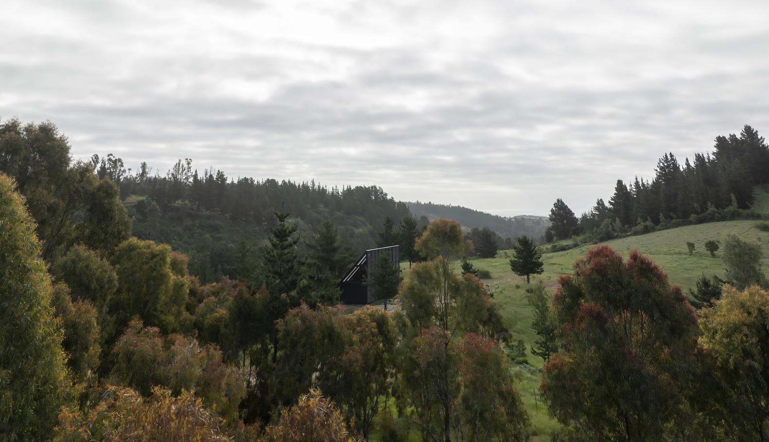 Long view of the dark volume emerging from sloping hillside with autumn foliage and rolling landscape