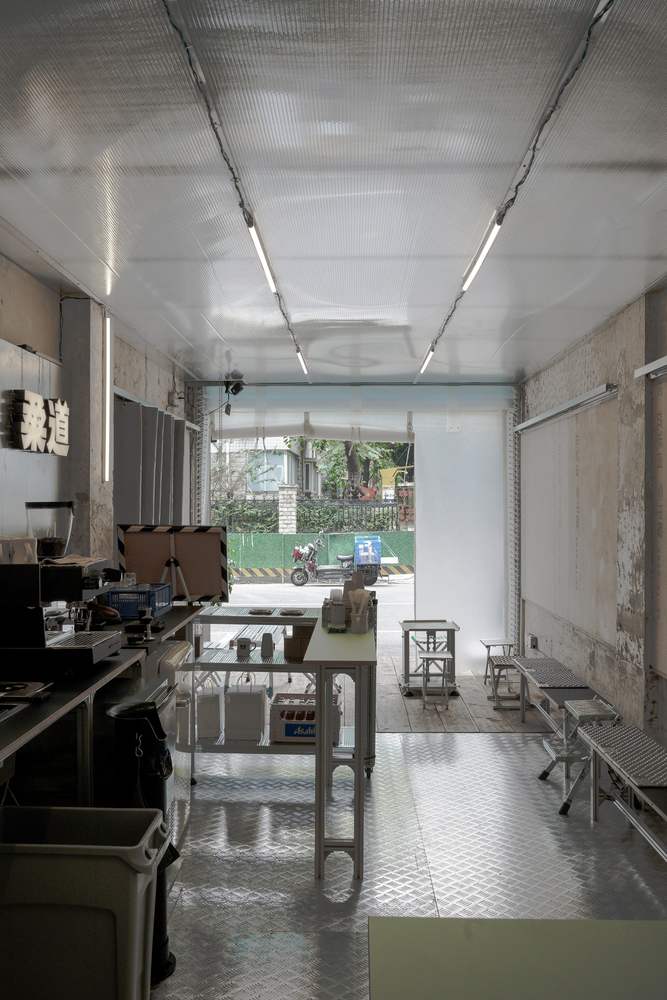 Workshop interior with corrugated metal ceiling and open storefront looking onto a tree-lined street