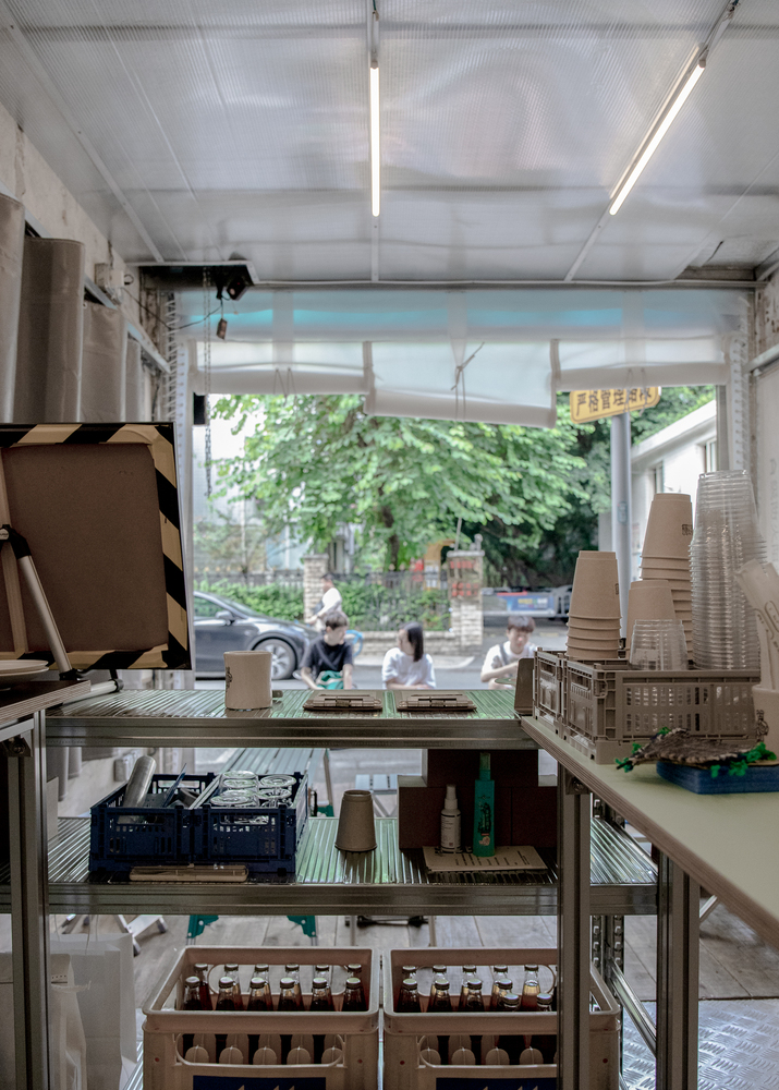 Metal shelving with cardboard model materials facing a glazed opening with pedestrians passing outside