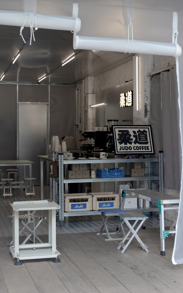 Coffee station setup with white duct overhead and metal shelving against unfinished concrete walls