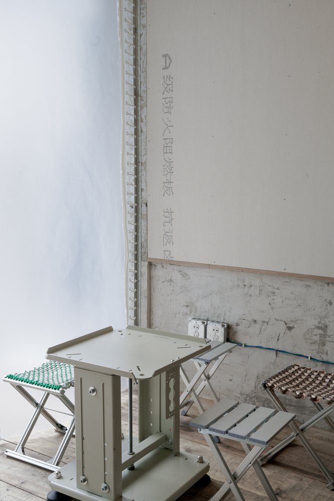 Corner of a room with plywood walls and folding metal stools with perforated seats