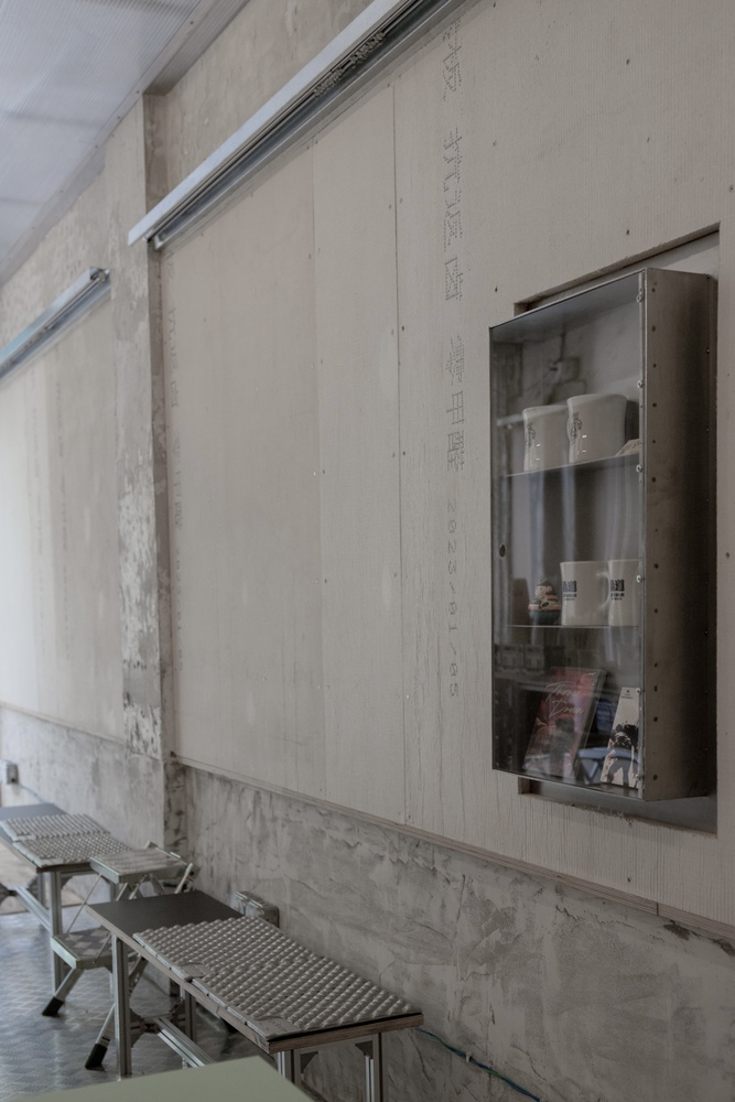 Plywood wall with metal display cabinet and folding stools along a concrete baseboard