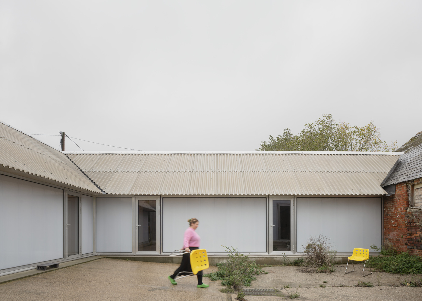 Courtyard facade with sliding glass doors and planted bed as a figure in motion carries a yellow crate