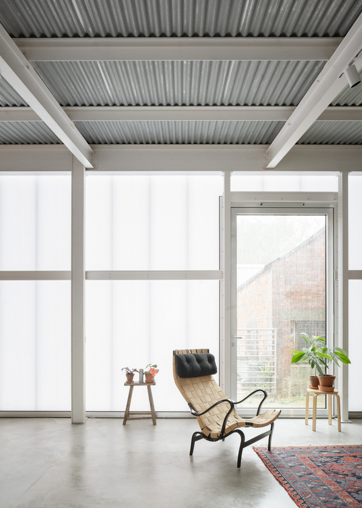 Polycarbonate wall panels with steel frame and corrugated metal ceiling above a woven chair on polished concrete