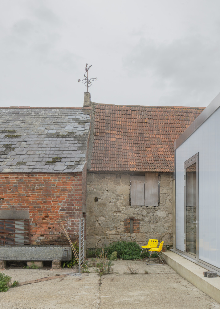 Courtyard with weathered brick barn, terracotta roof, weather vane and yellow chairs under overcast sky