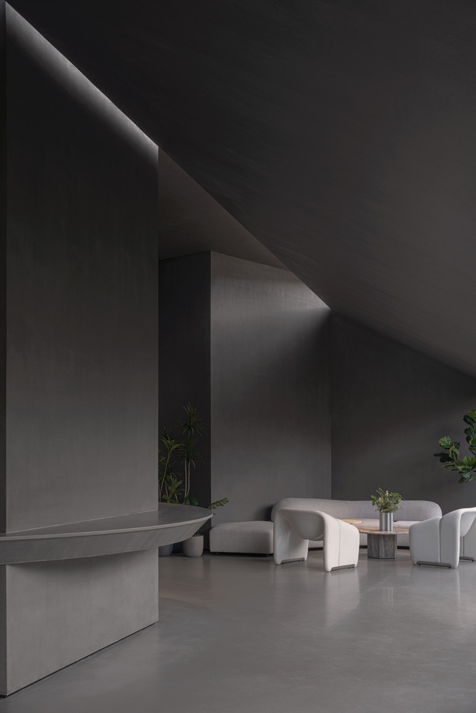 Reception lobby with angled wall planes, pale stone flooring and seating clusters beneath indirect light