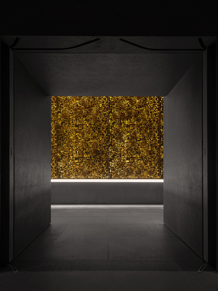 Perforated golden metal screen wall illuminated from behind in a darkened interior gallery space