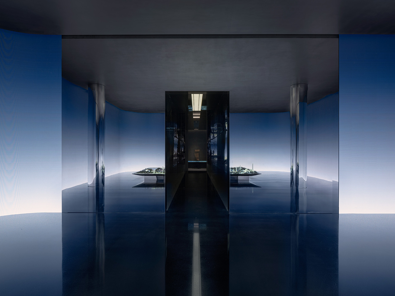 Symmetrical corridor with reflective blue floor and dark ceiling opening to a bright courtyard beyond
