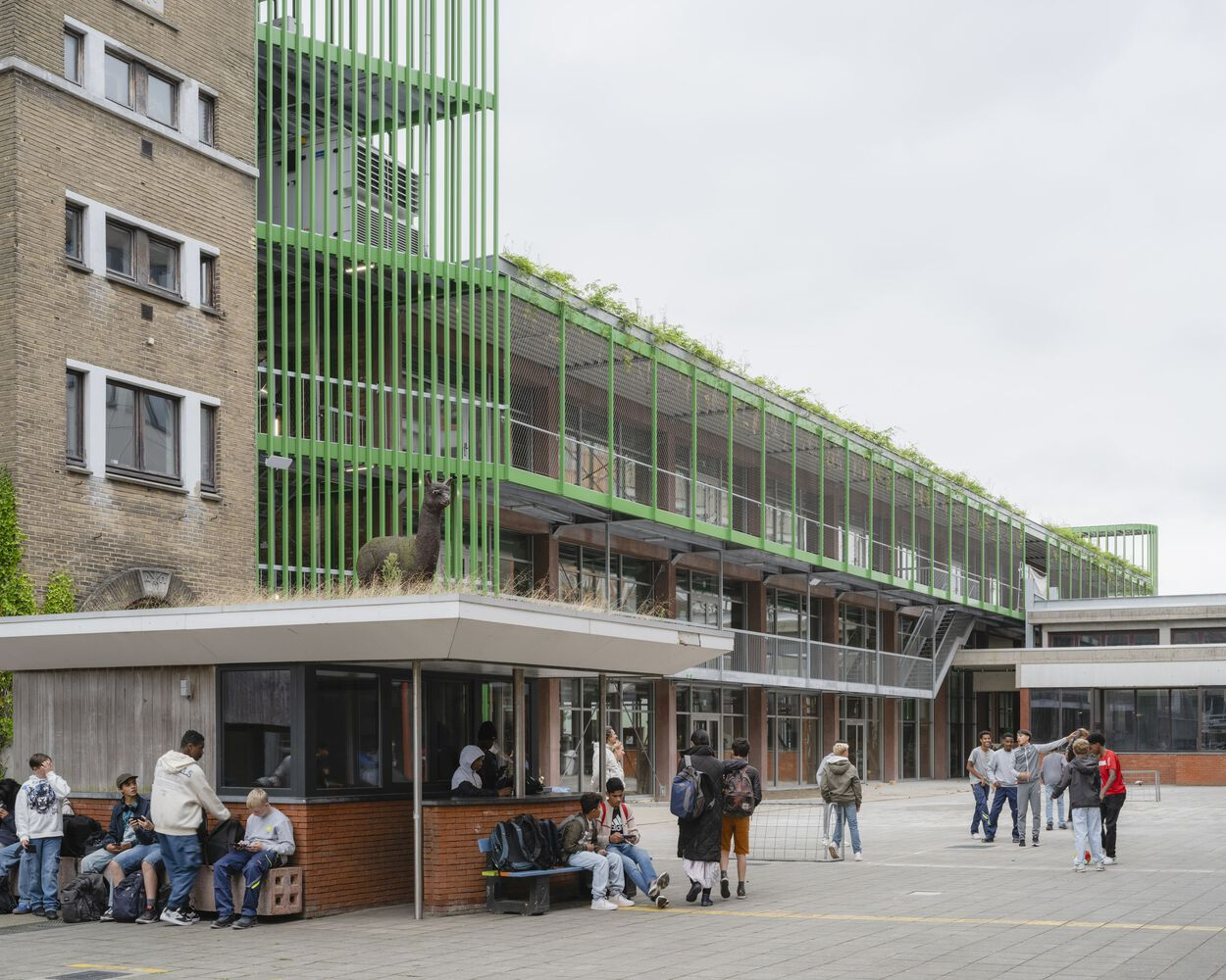 Courtyard view showing green vertical brise-soleil tower and glazed walkway with students gathering below