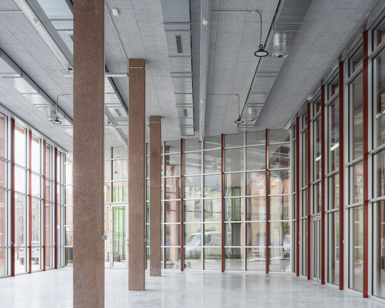 Interior corridor with exposed concrete ceiling, cork-clad columns and red-framed glazed partitions