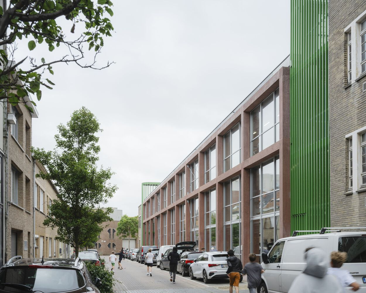 Street view of the glazed facade with red framing alongside parked cars and pedestrians