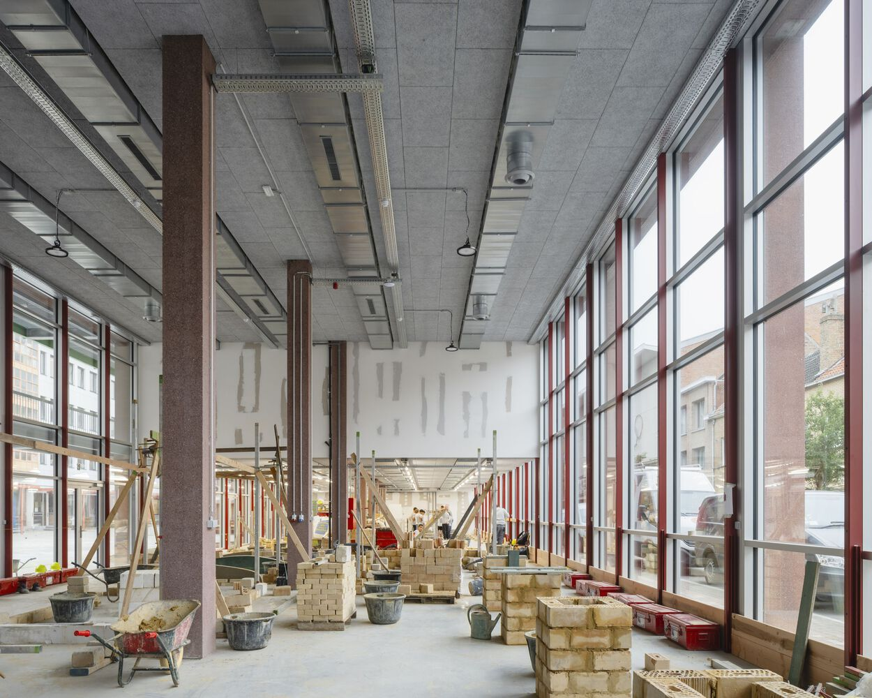 Ground floor interior with exposed concrete ceiling, steel columns, and red-framed glazing during construction
