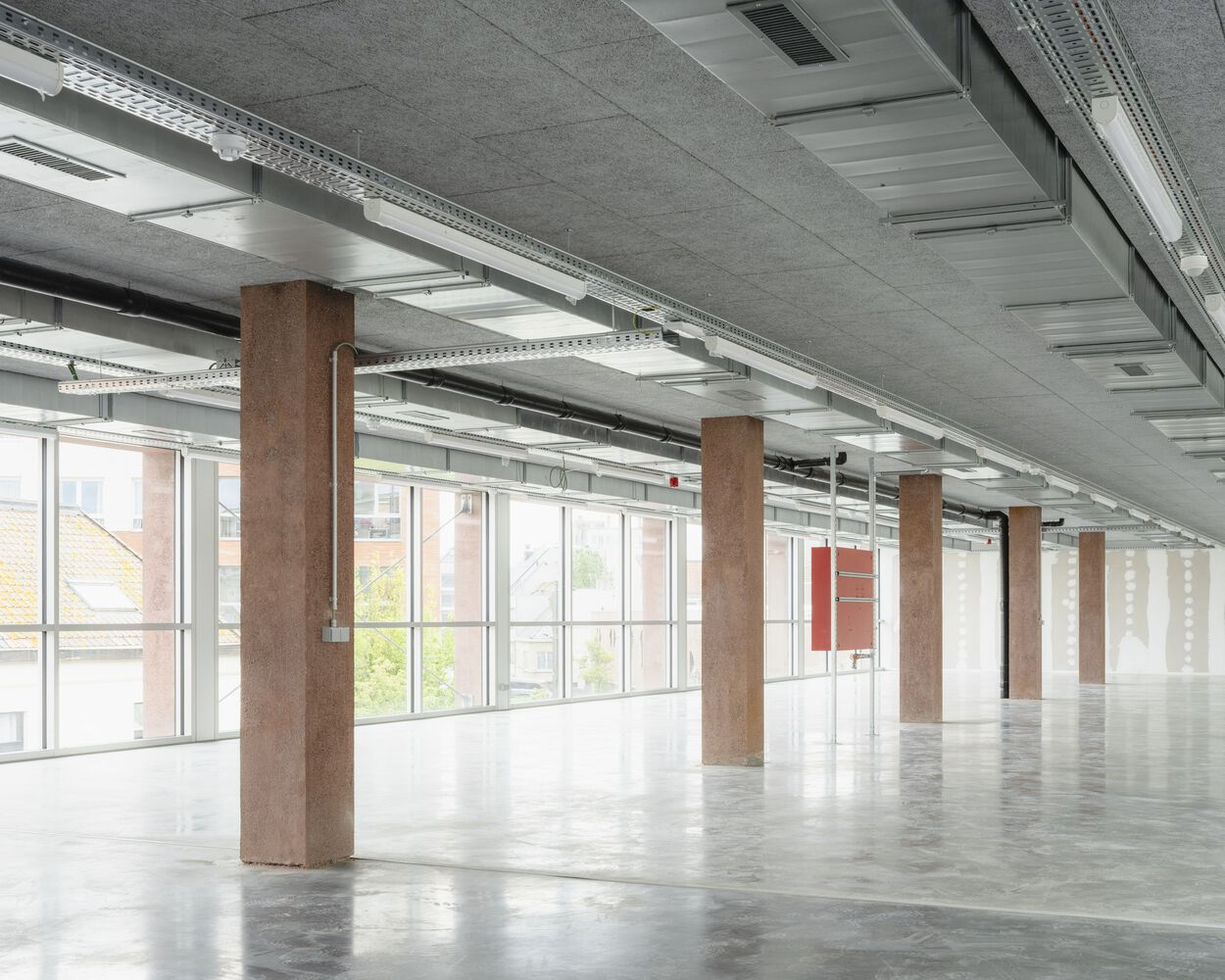 Open floor plate with polished concrete flooring, steel columns, and continuous glazed facade admitting daylight