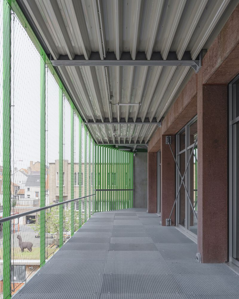 Covered balcony with corrugated metal ceiling, green vertical louvres, and grated metal flooring overlooking rooftops