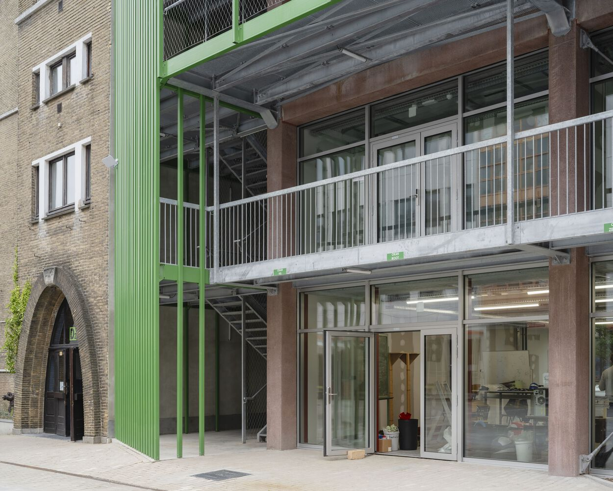 Street-level view of the green steel-framed entrance canopy and white vertical balusters on the upper balcony