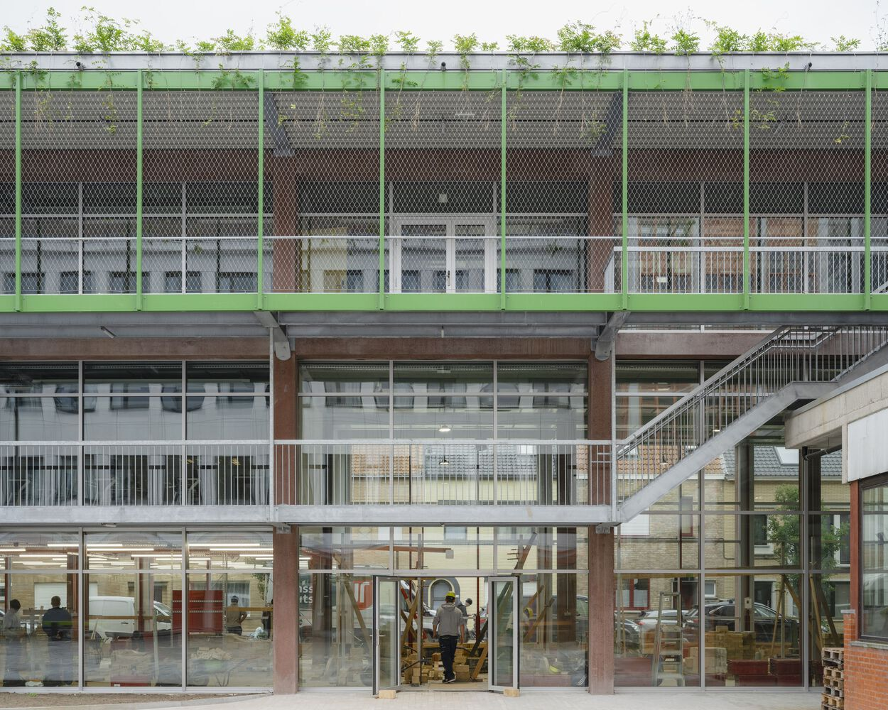 Facade showing three stacked levels with mesh-paneled screens, rooftop planting beds, and full-height glazing