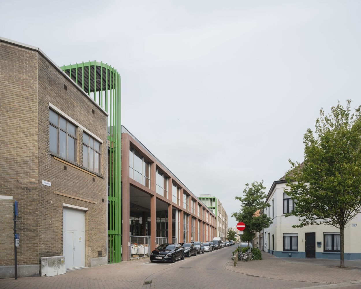 Long street facade with repetitive steel window frames and green tubular towers flanking the entrance under cloudy weather