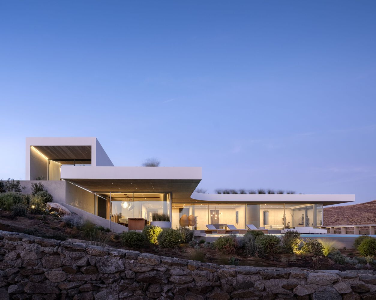Exterior view of the white cantilevered volumes on a terraced stone base at dusk