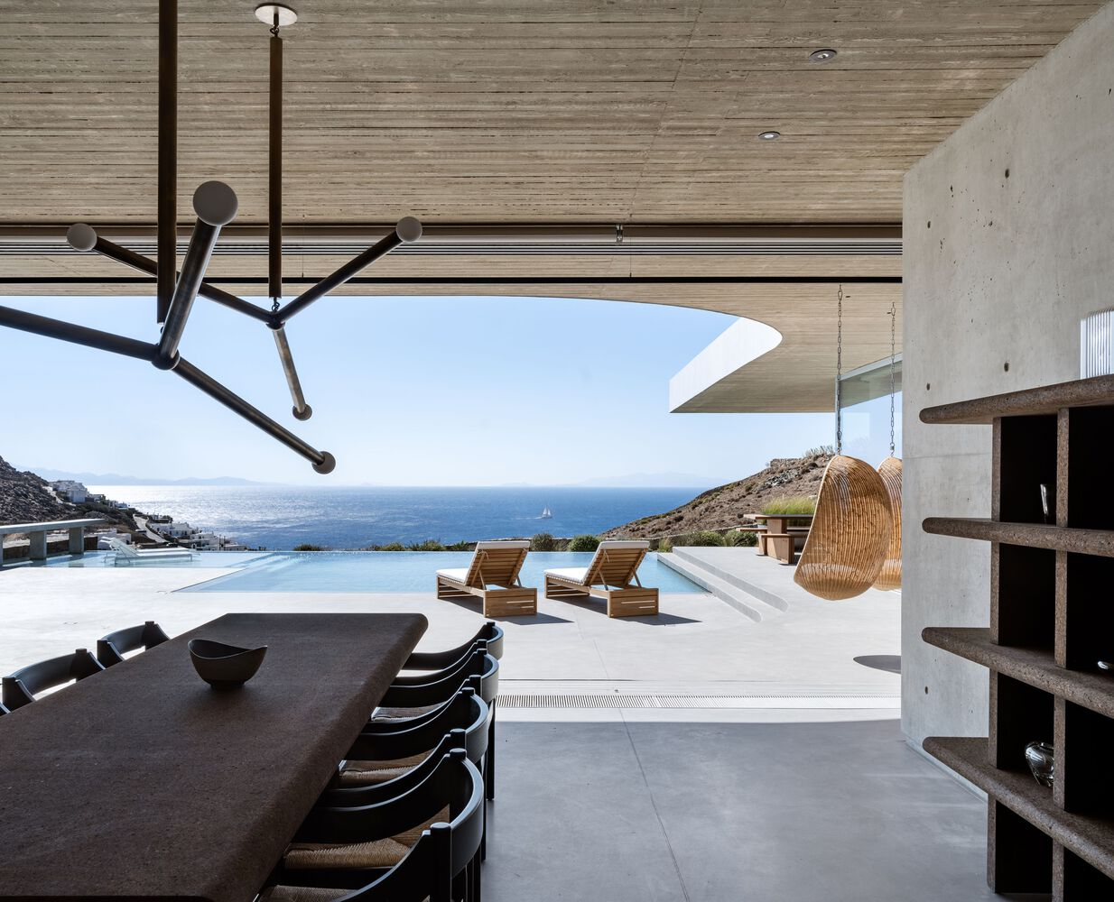 Living area with timber ceiling and infinity pool overlooking the ocean under clear sky