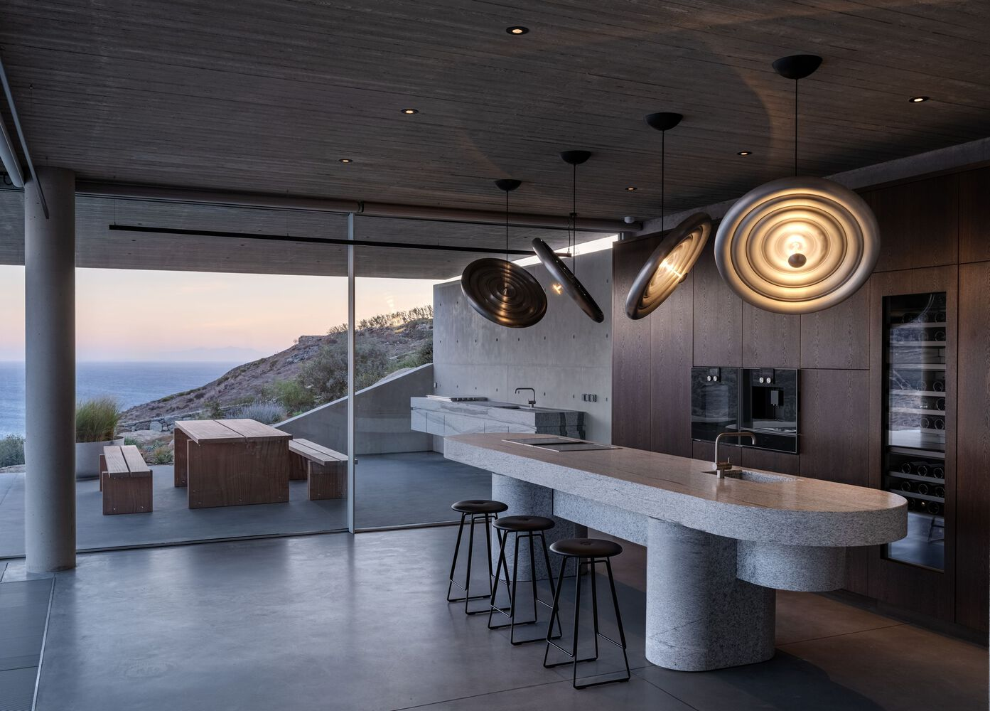 Kitchen island with curved stone counter and pendant lights opening to terrace at twilight