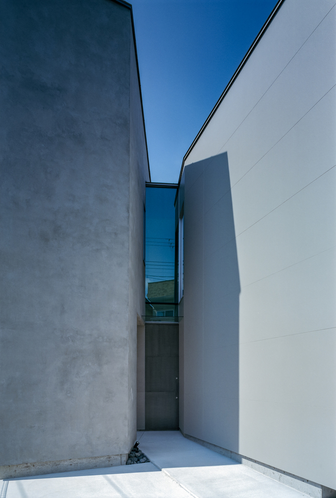 Narrow exterior passage between two concrete walls open to blue sky above